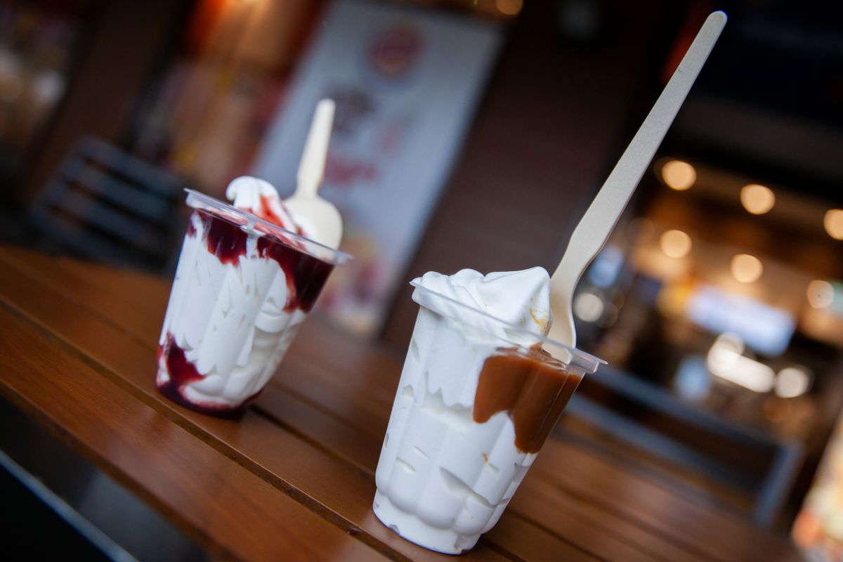 Two soft-serve ice cream sundaes sit on a wooden counter inside a casual restaurant
