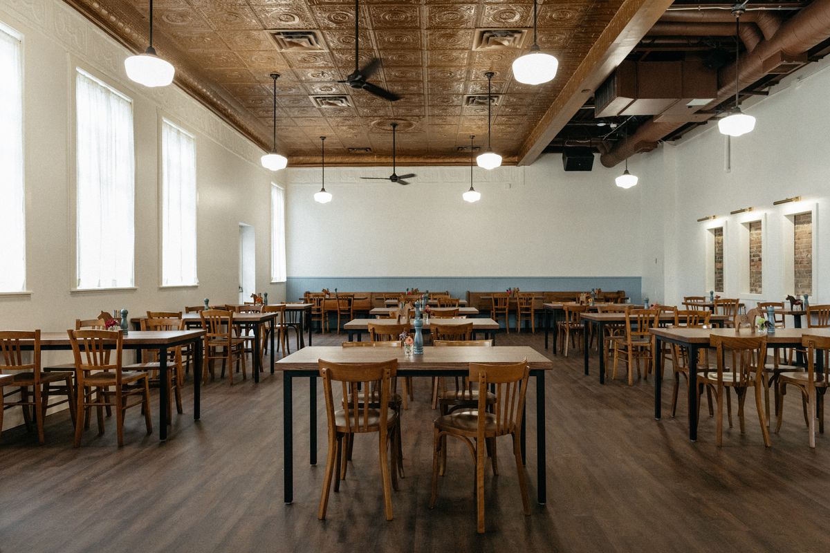 A large dining room with white walls and wooden tables and chairs. 