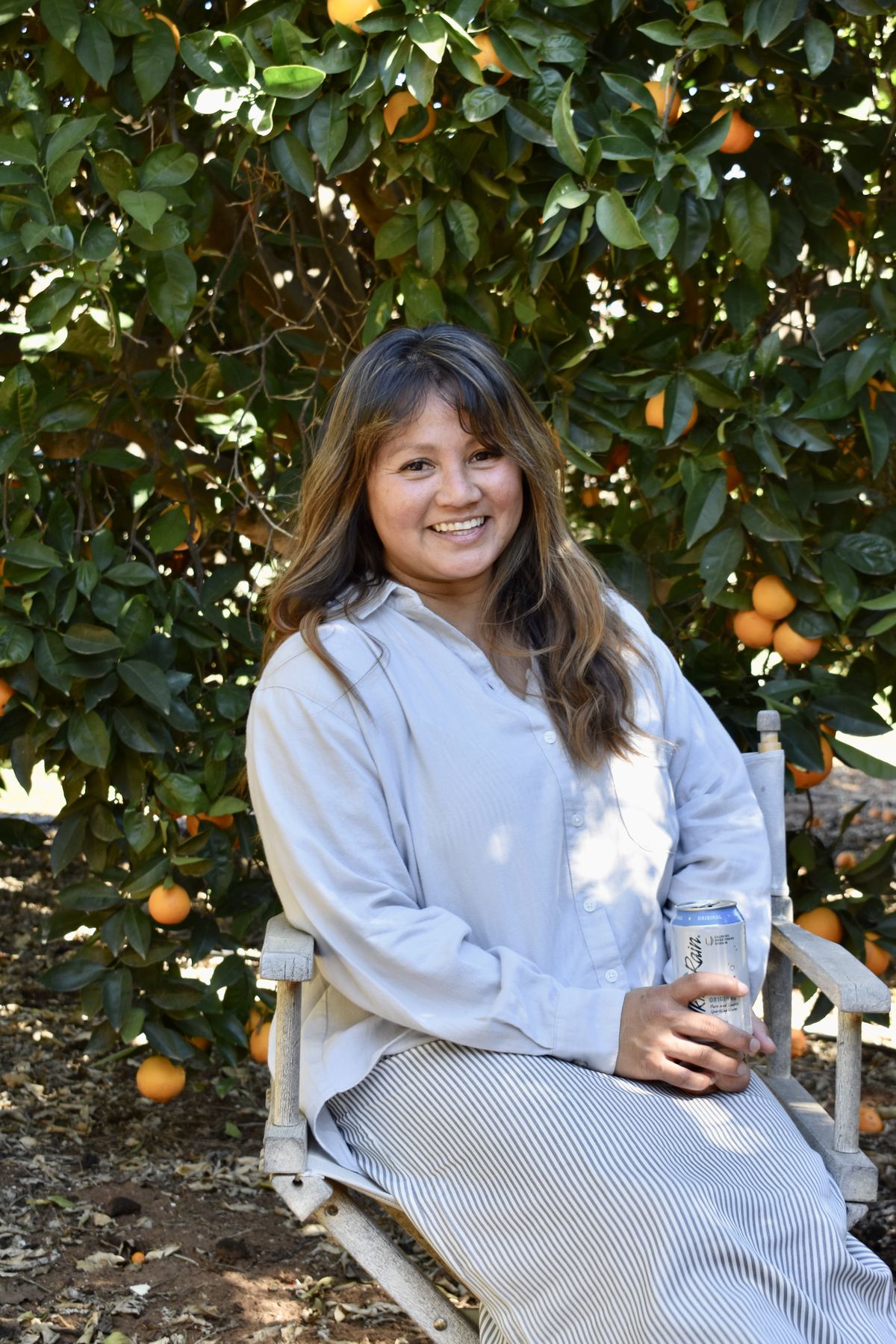 A woman sits in front of an orange tree.