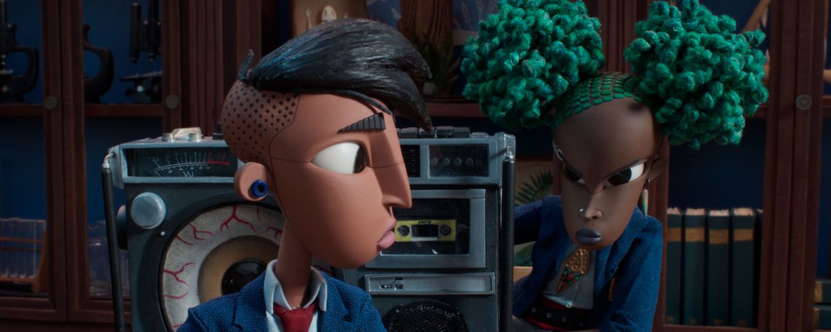 Raúl, a trans Latinx teenager with an undercut, sits in a school classroom at a desk looking back at Kat, a Black 13-year-old punk girl with bright green hair and a giant boombox, in the stop-motion animated film Wendell &amp; Wild