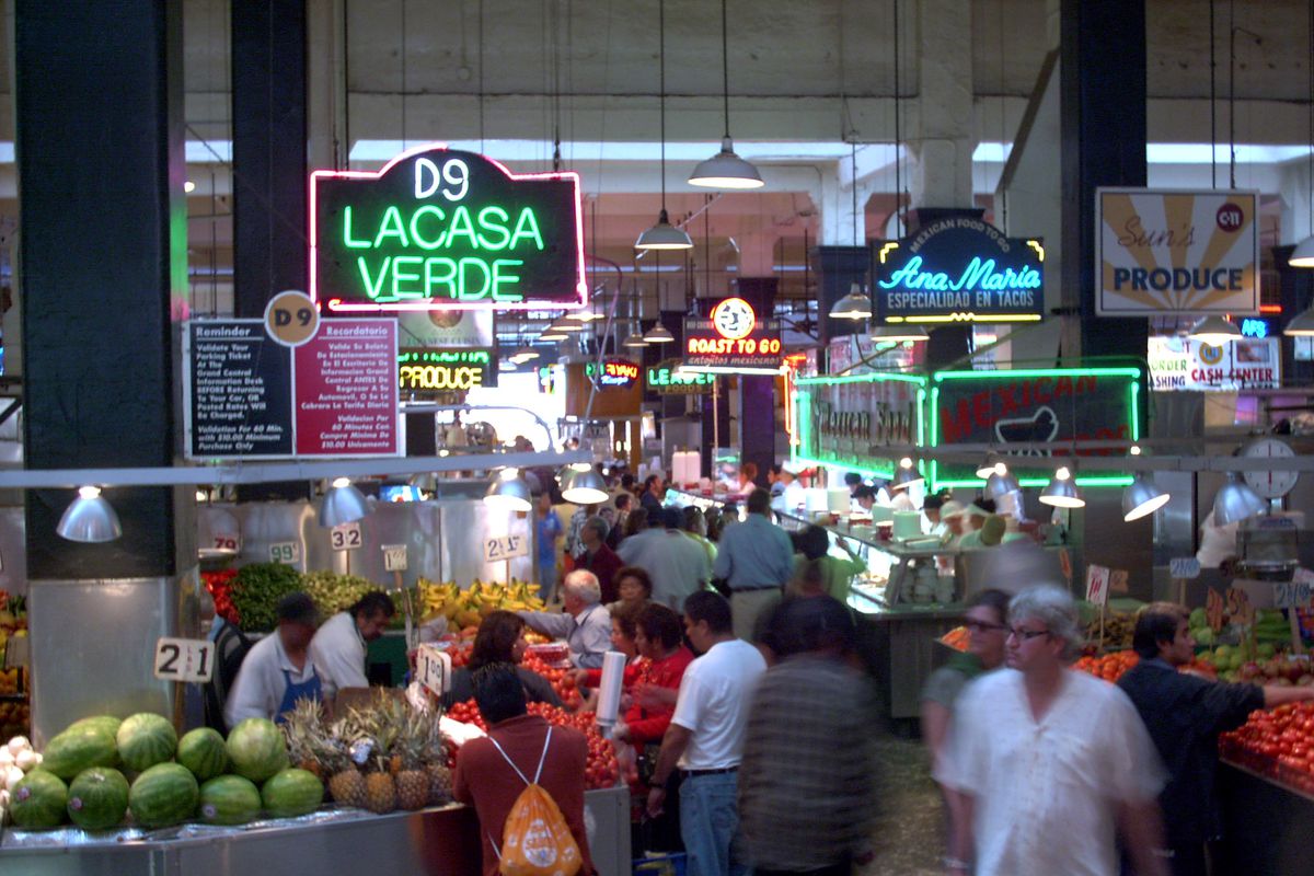 A public market teems with customers and neon signs at daytime.