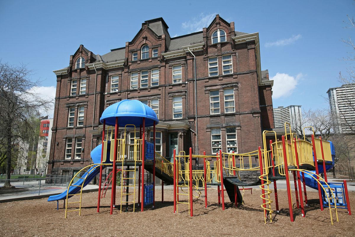 A colorful playground setup in front of an old brick school building.