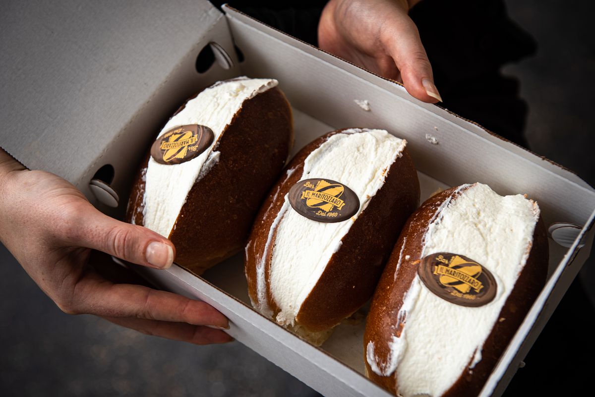 Hands hold a box of cream-stuffed pastries topped with edible logos for Il Maritozzaro.