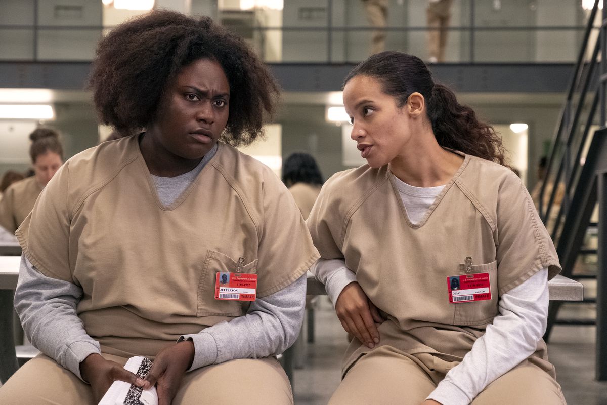 Two characters in the TV show “Orange Is the New Black,” Taystee and Daya, wear prison uniforms and talk to one another.