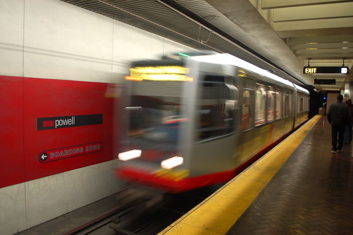 The front of a Muni light-rail train, blurred as it accelerates into a station stop.