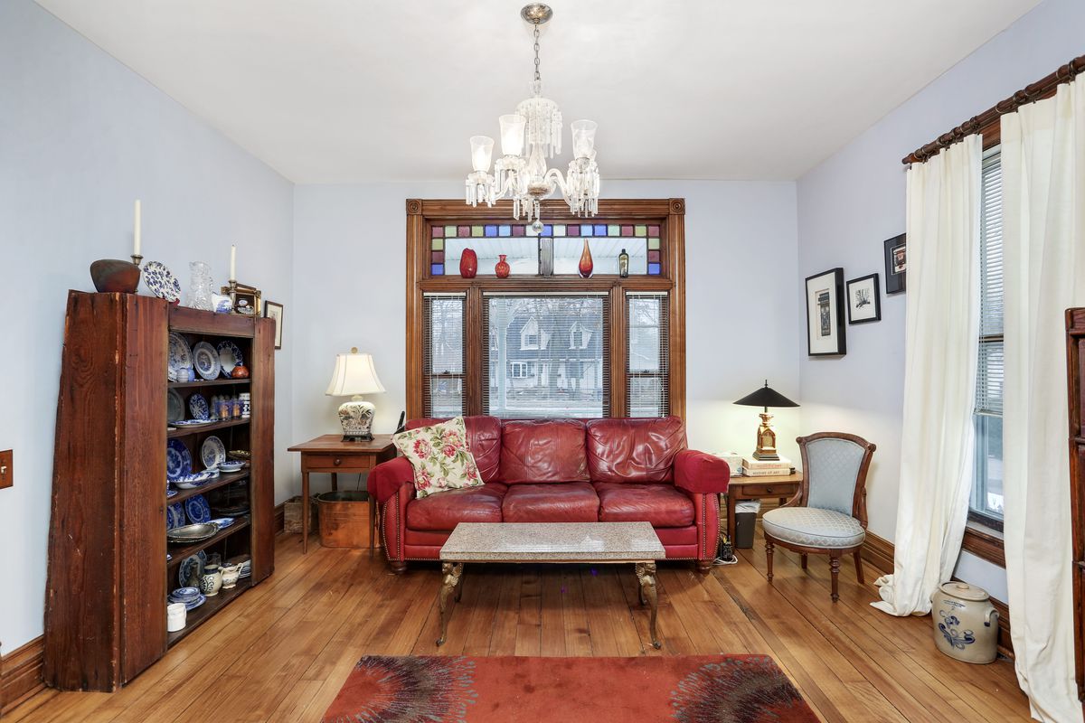 A view of the living room with hardwood floors and stained glass windows. A red leather couch sits under the windows.