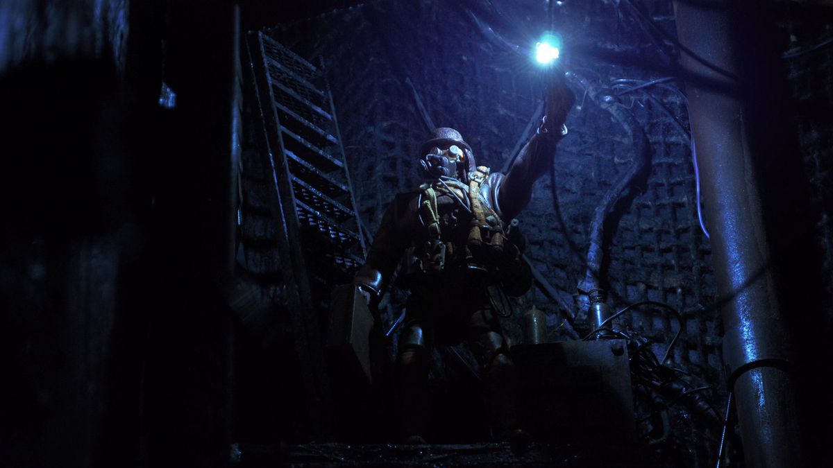 An assassin wearing a gas mask holds a light in a dark underground corridor in Mad God.