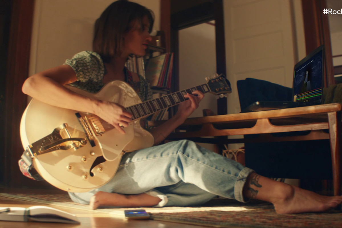 a woman sitting on the floor playing an electric guitar in a trailer for Rocksmith Plus