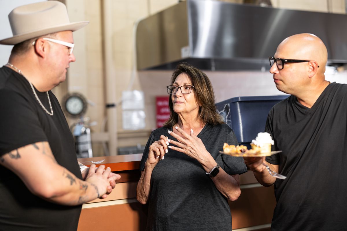 Two men talk to an older woman who stands in between them. The man on the right holds a plate with a fried pie and ice cream on it.