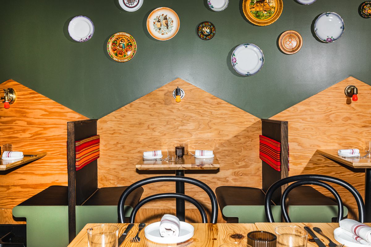 A dining room with dark green walls and exposed wood booths. Decorative plates adorn the walls.