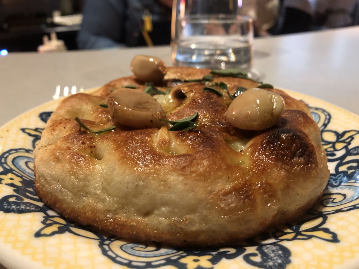 A round, puffy baked bred with garlic and herbs on top, set on a yellow and blue patterned plate.