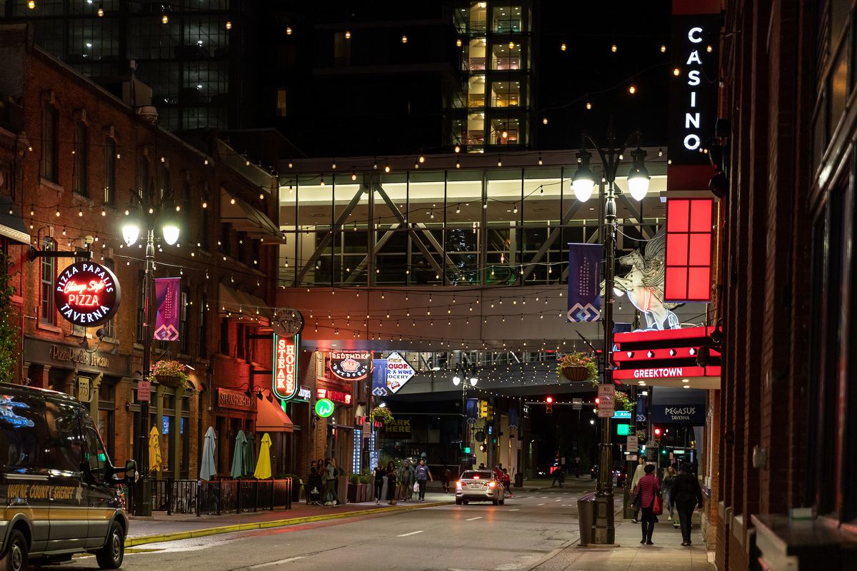 Restaurant signs are shown along the street next to the Greektown Casino at night.