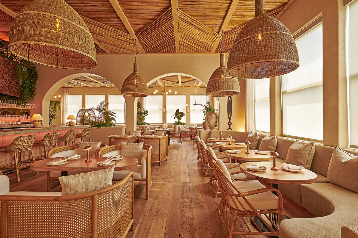 A golden dining room with wooden floors, curved banquettes, and wicker covered hanging lamps.