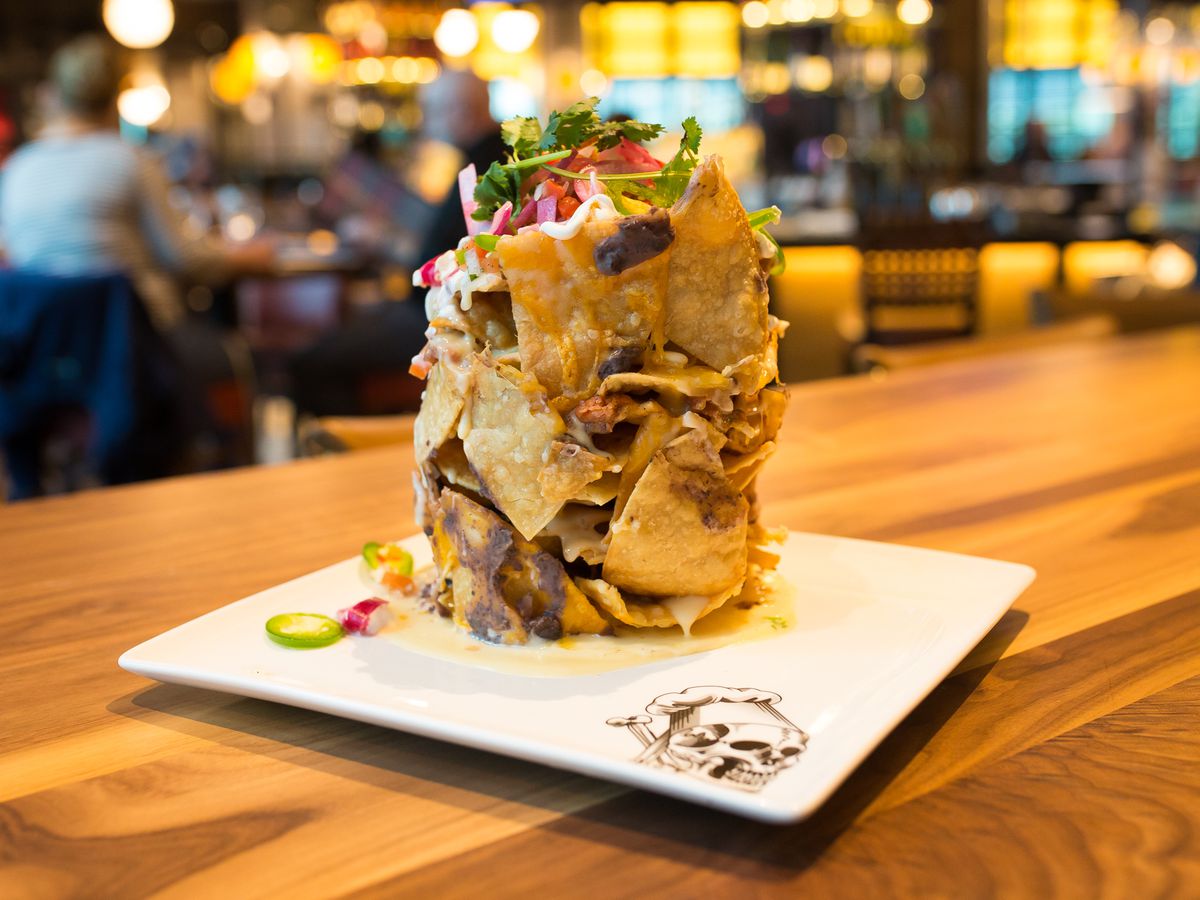 A pile of “trash can nachos” on a white plate on a wooden table in a restaurant.