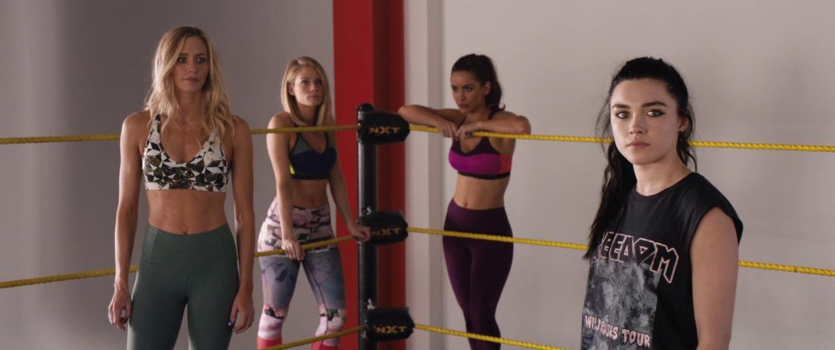 Florence Pugh has a goth vibe and wears black in a wrestling ring, with other female wrestlers with a jock-ier vibe standing behind her.