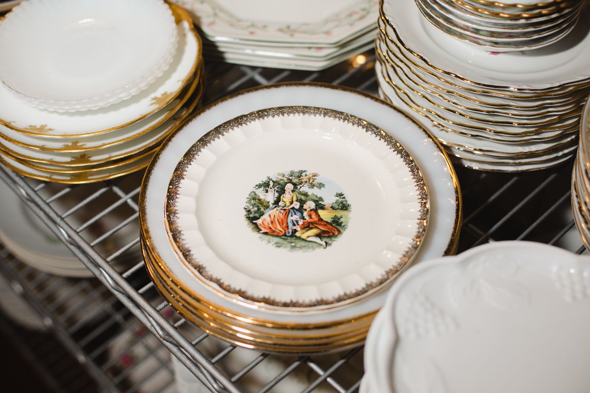 Stacks of gold-rimmed plates with a vintage painted design of people in the countryside in the middle.