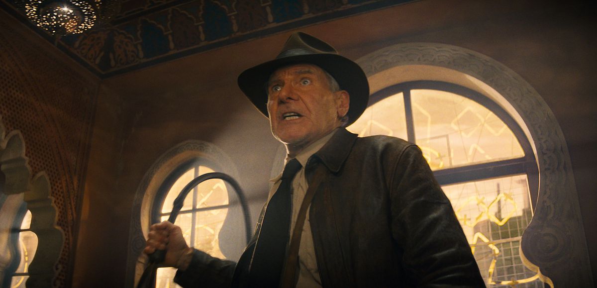 Indiana Jones (Harrison Ford) looks harried and shaken as he lifts his trademark whip in a fight while standing silhouetted against a bright window in Indiana Jones and the Dial of Destiny