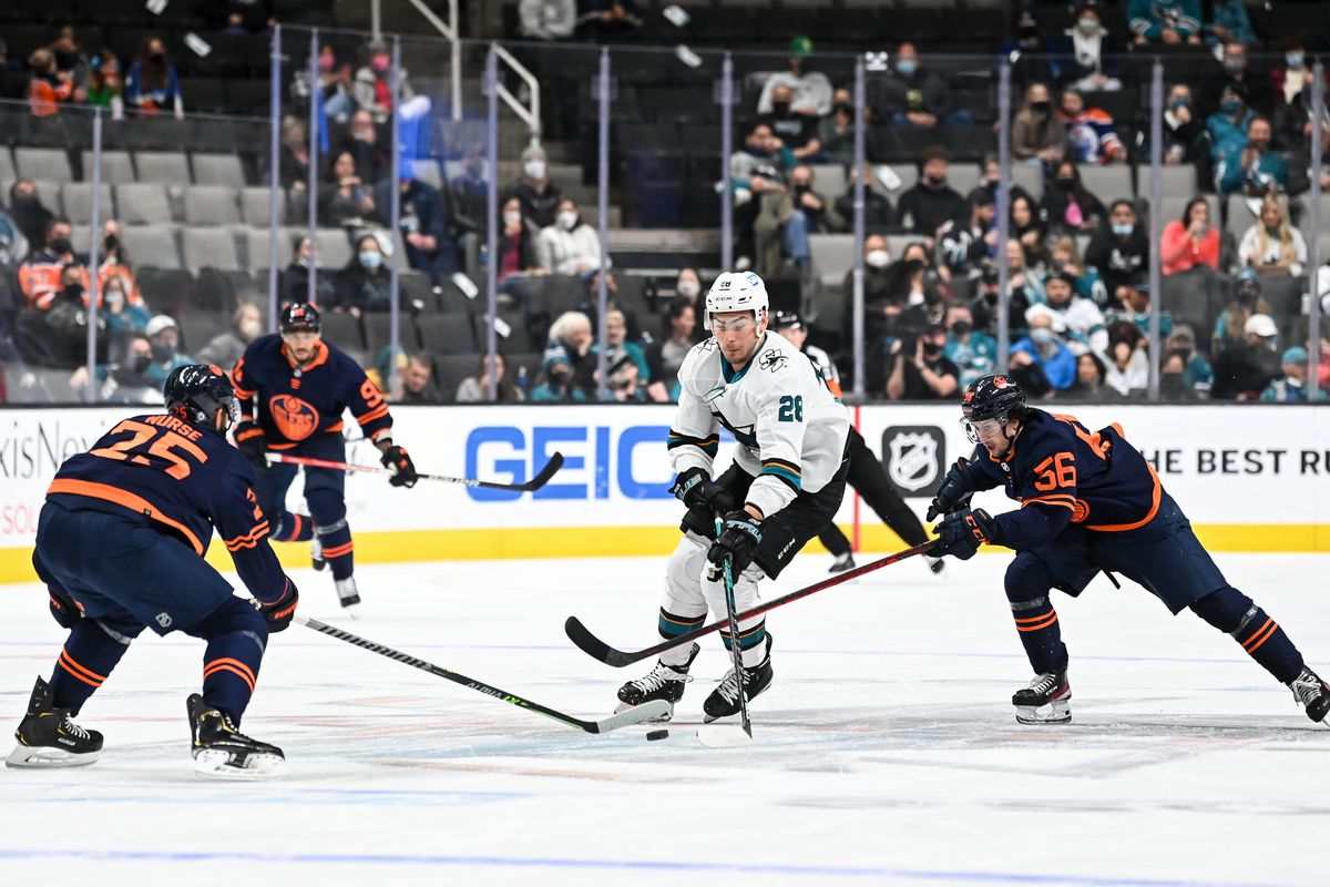 Timo Meier #28 of the San Jose Sharks skates ahead with the puck against Darnell Nurse #25 and Kailer Yamamoto #56 of the Edmonton Oilers in a regular season game at SAP Center on February 14, 2022 in San Jose, California.