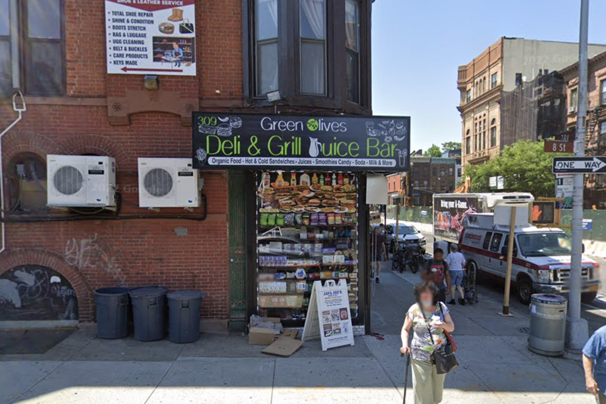 A red brick building with a corner bodega with a sign that reads Green Olives Deli &amp; Grocery.