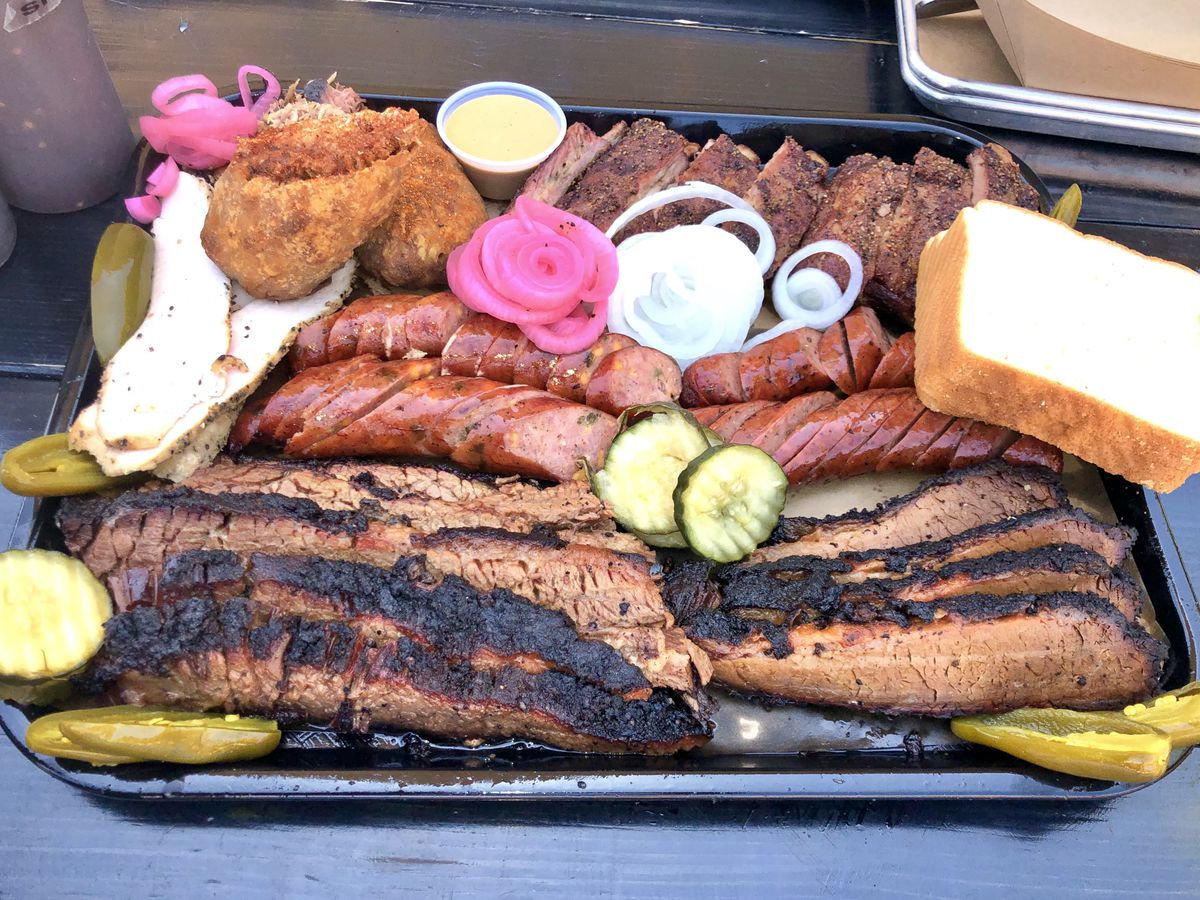 A tray of barbecue holds links of sausage, sliced brisket, pickles, and bread.
