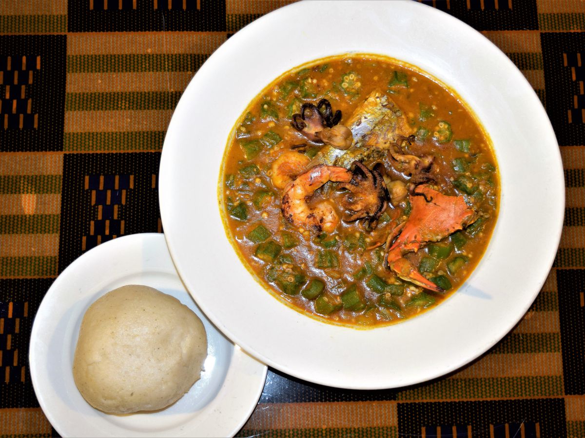 A seafood okra stew in a white bowl next to fufu at Appioo
