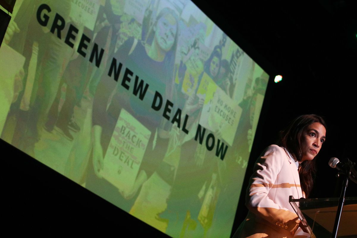 Rep. Alexandria Ocasio-Cortez onstage in front of a backdrop that reads, “Green New Deal Now.”