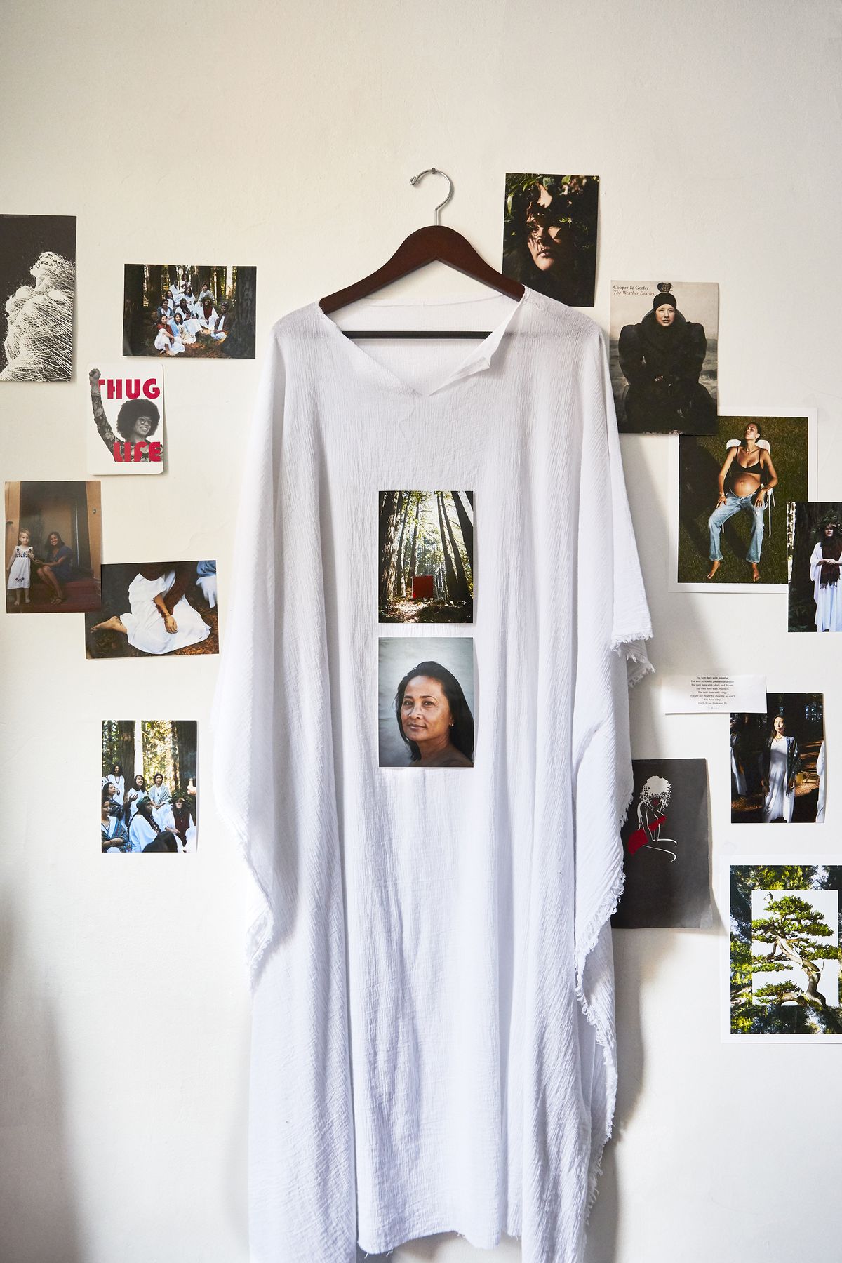 A white gown hangs on the wall and it’s surrounded by color photos.