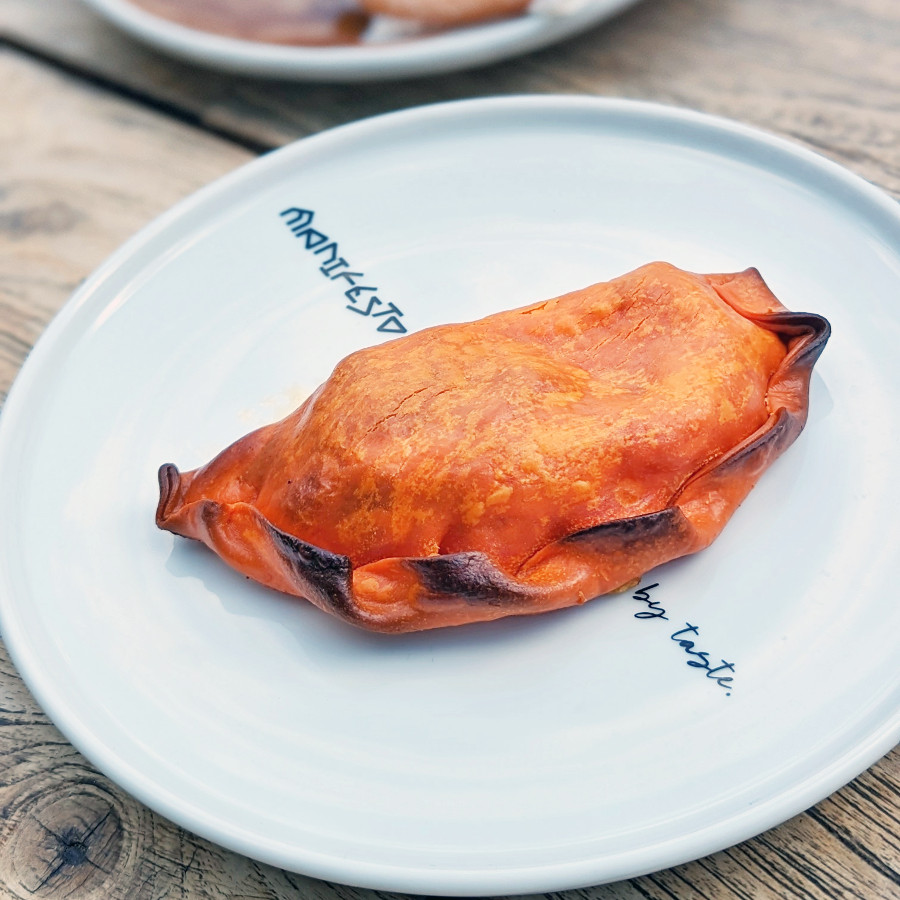 An empanada presented on a bright white plate on a wooden picnic table.