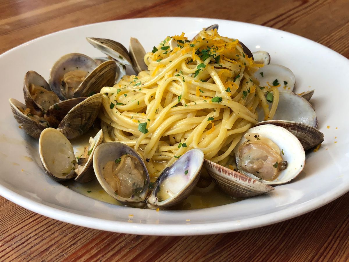 Parsley-flecked linguini pasta with clams and olive oil atop a white plate.