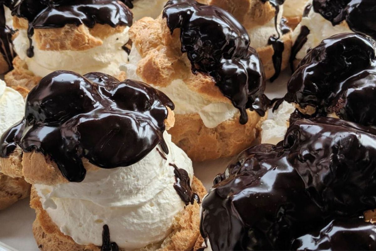 Closeup of a tray of cream puffs, each topped with shiny chocolate sauce