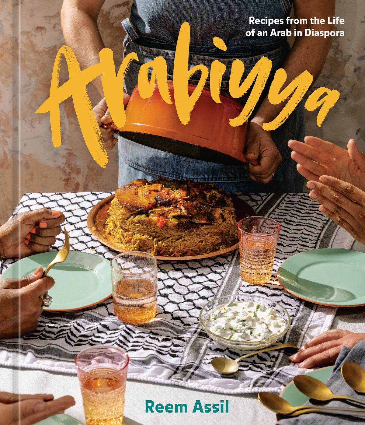 The cover of Arabiyya: At the head of a brightly decorated table, a rice dish is served from an overturned pot.