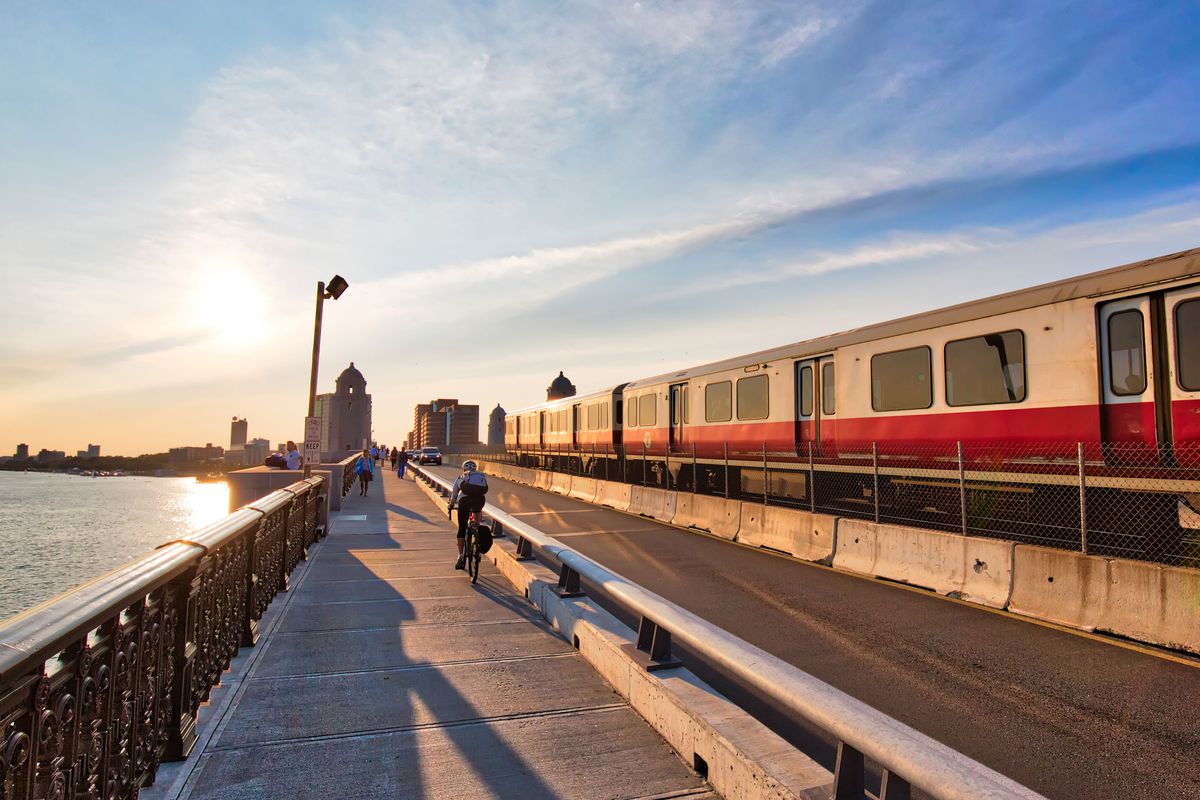 Boston train rides on a track with a view of a river on the left side along with a sunset.