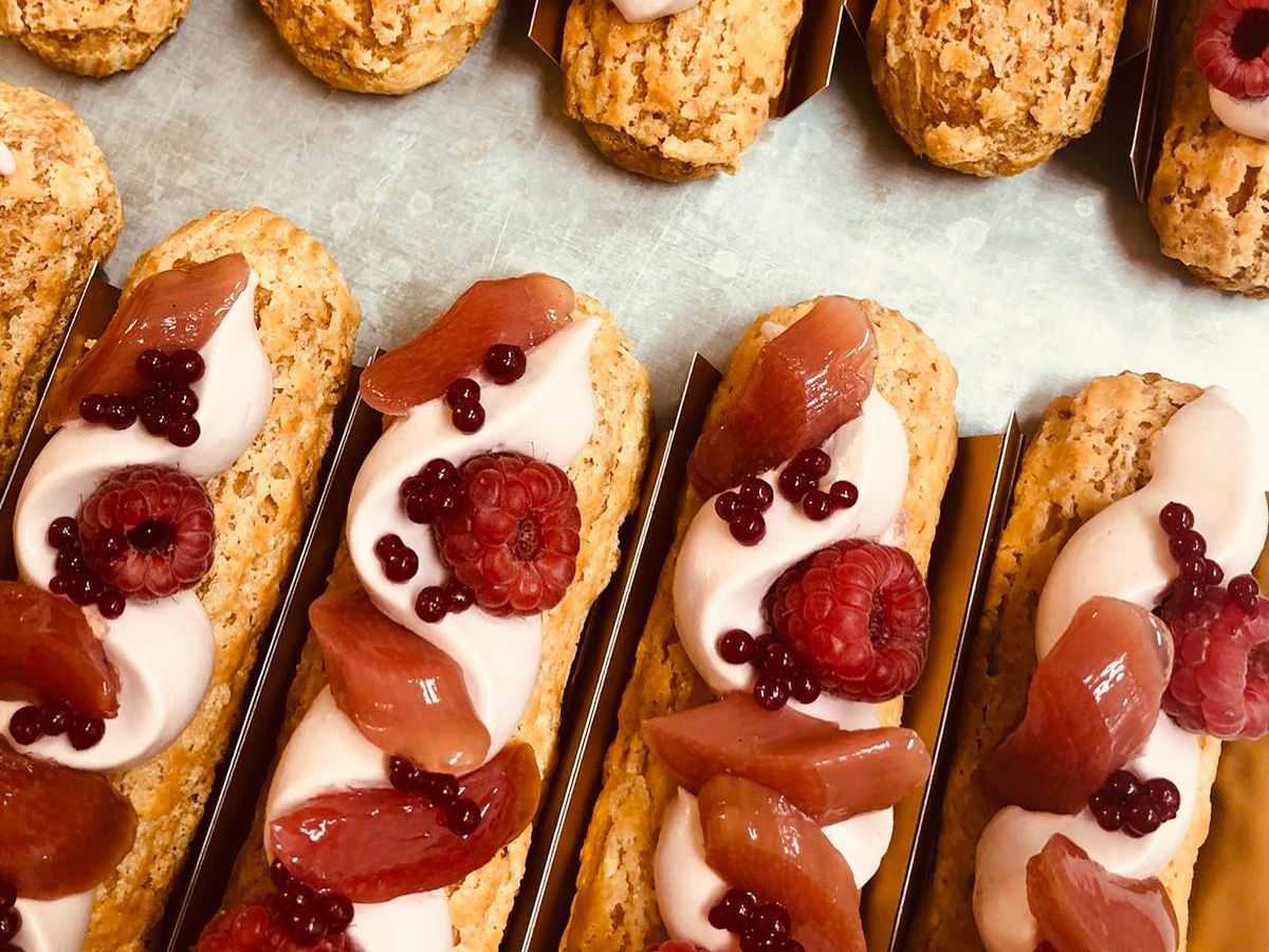 From above, rows of ornate eclairs topped with slices of rhubarb and raspberries