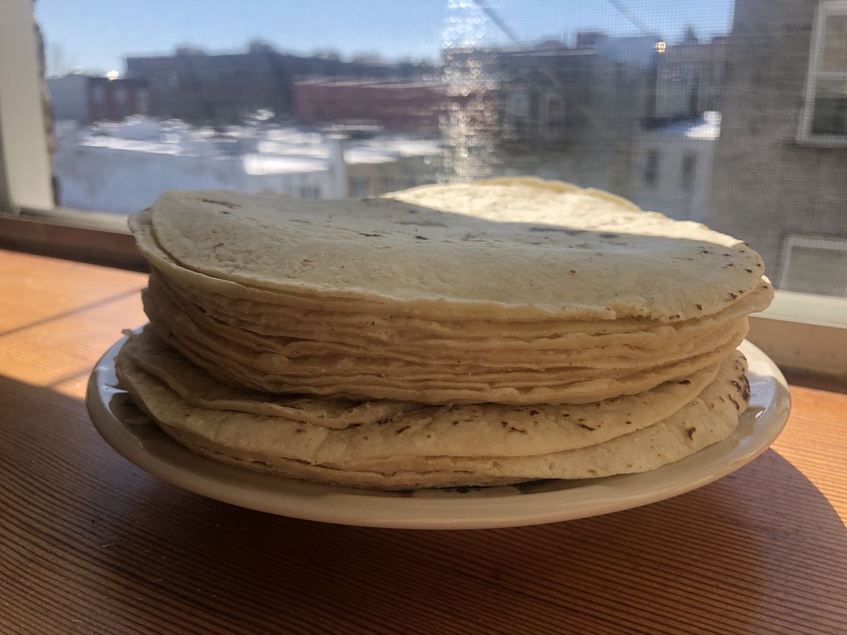 A plate of stacked tortillas is placed in the sun on a wooden windowsill