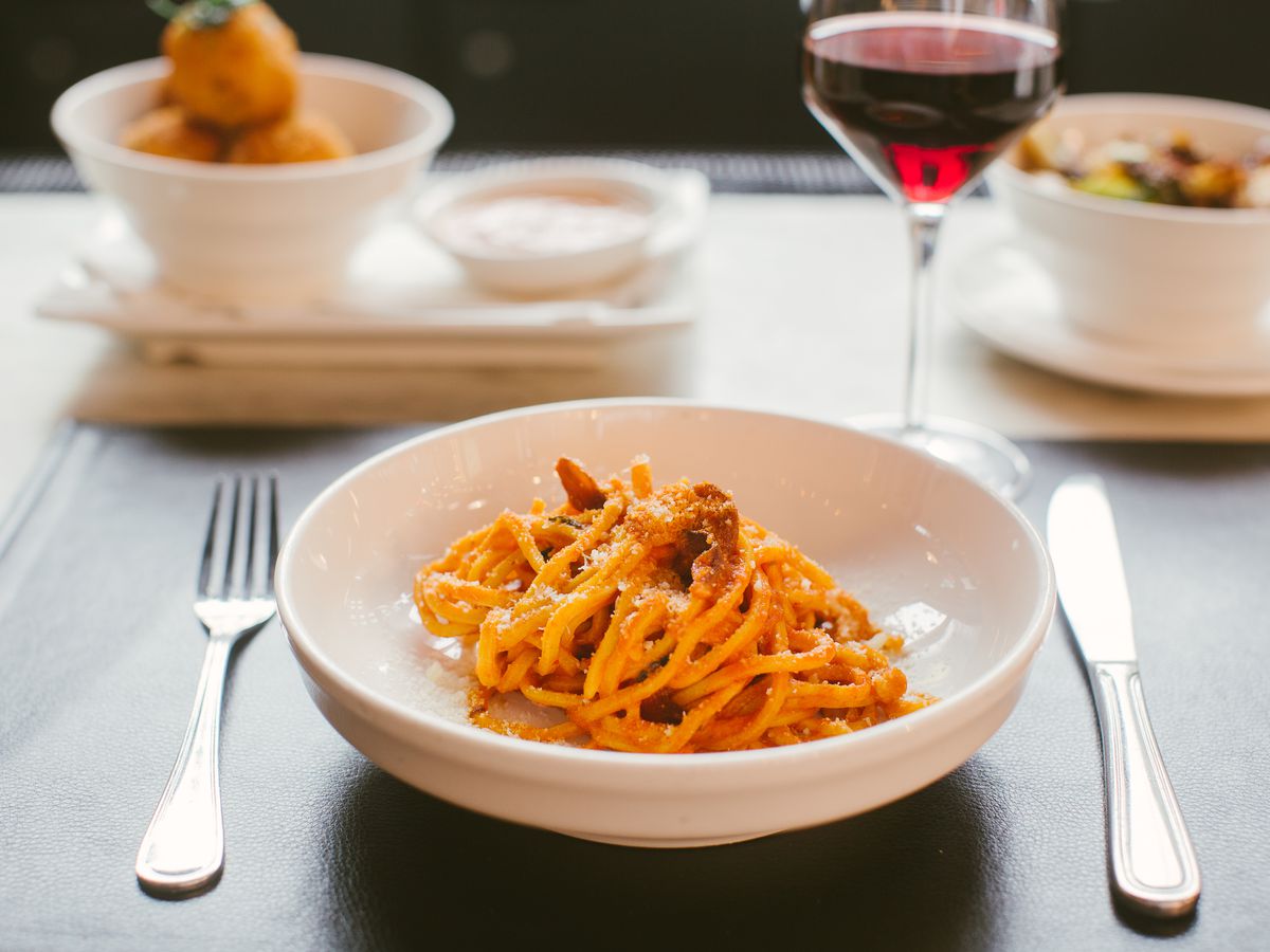 Spaghetti arrabbiata sits in a bowl next to a glass of red wine on a black placemat