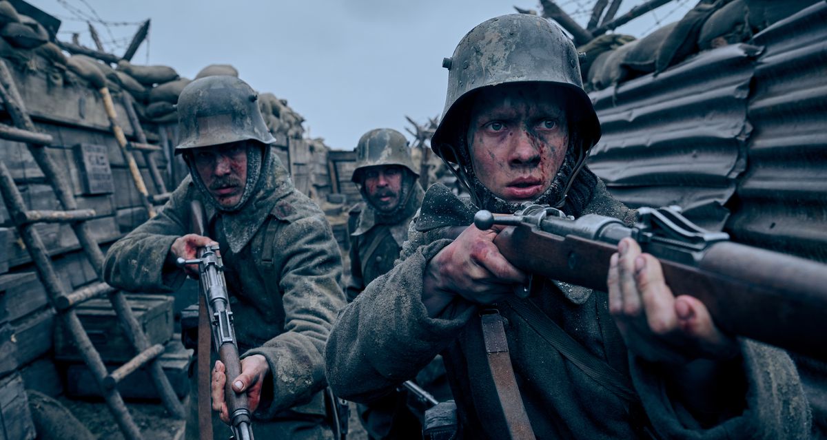 Three blood-and-mud-smeared soldiers fearfully navigate a World War I trench with their rifles out in Netflix’s Best Picture nominee All Quiet on the Western Front