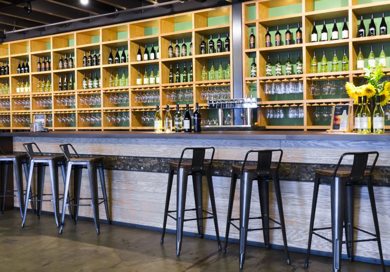 A bar with rows of wine bottles on the back bar and metal stools