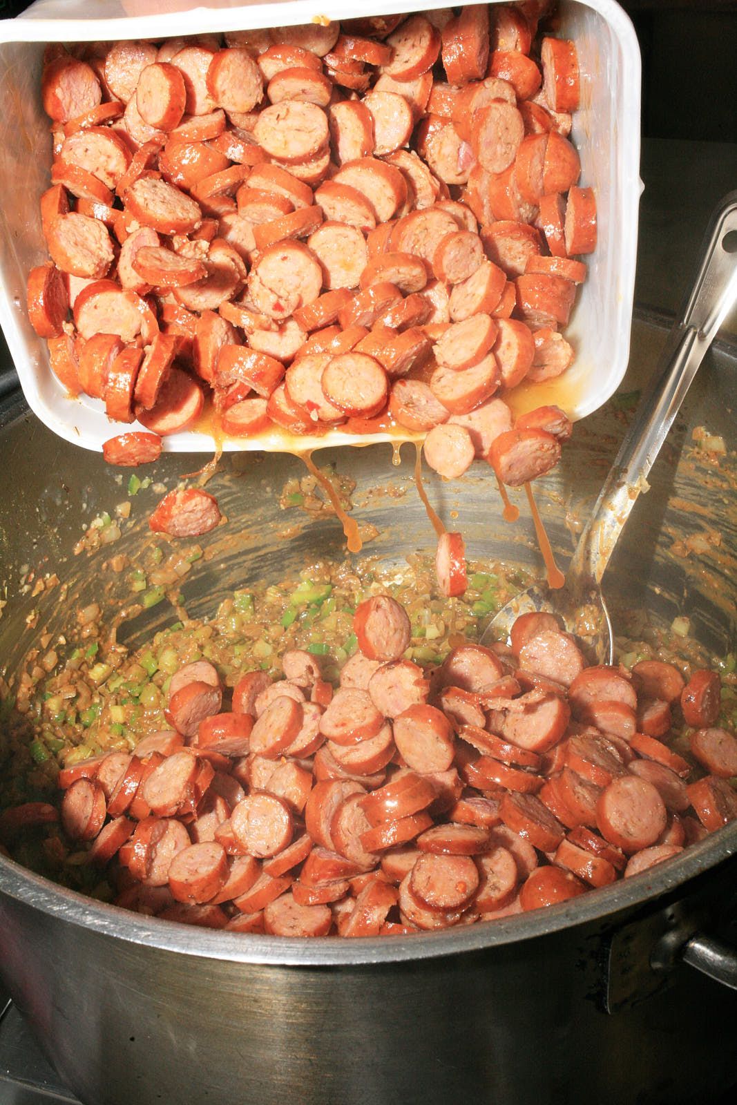 A tub of andouille sausage, cut into coins, is poured into the gumbo pot.