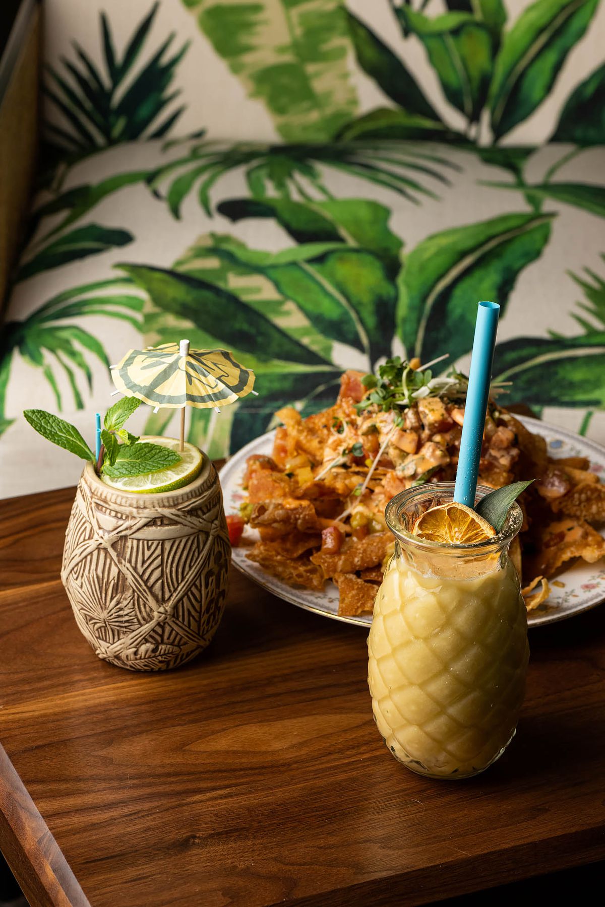 Food and cocktails on a wooden table in fun vessels at a tiki restaurant.