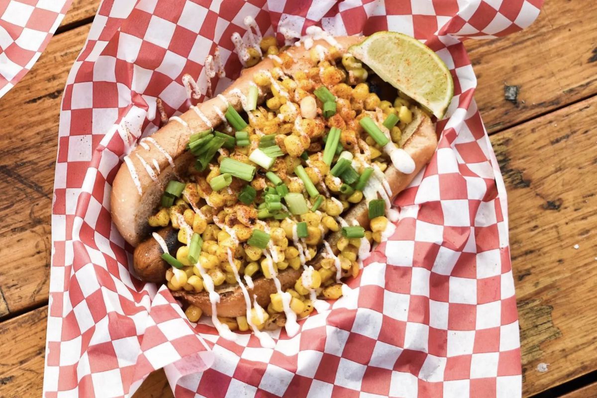 A hot dog topped with corn and scallions and a white sauce.