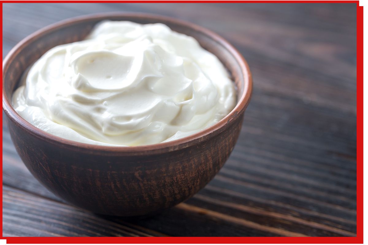 A small wooden bowl of creme fraiche sits on a dark wooden table.
