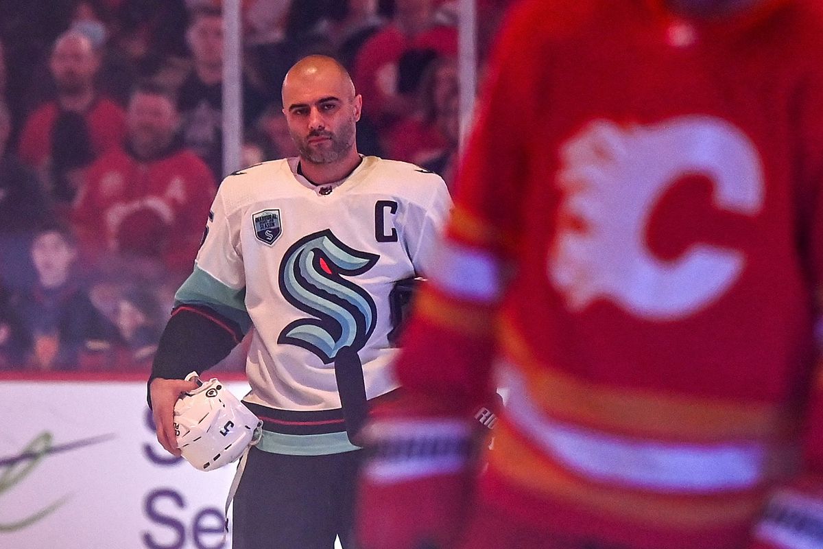 Mark Giordano, foregrounded by a Flames player, stands in the dimmed light of the Saddledome during the performance of the national anthems