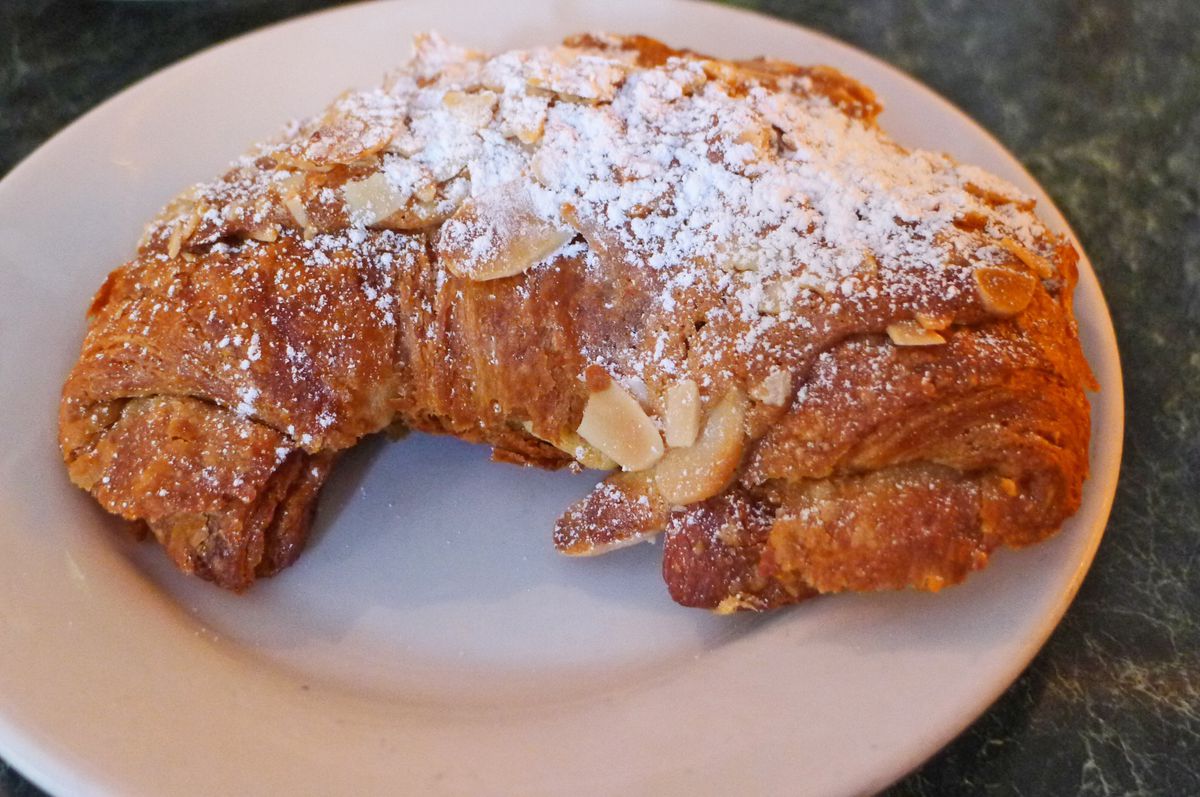 A crescent shaped pastry on a white plate, covered with powdered sugar and almonds.