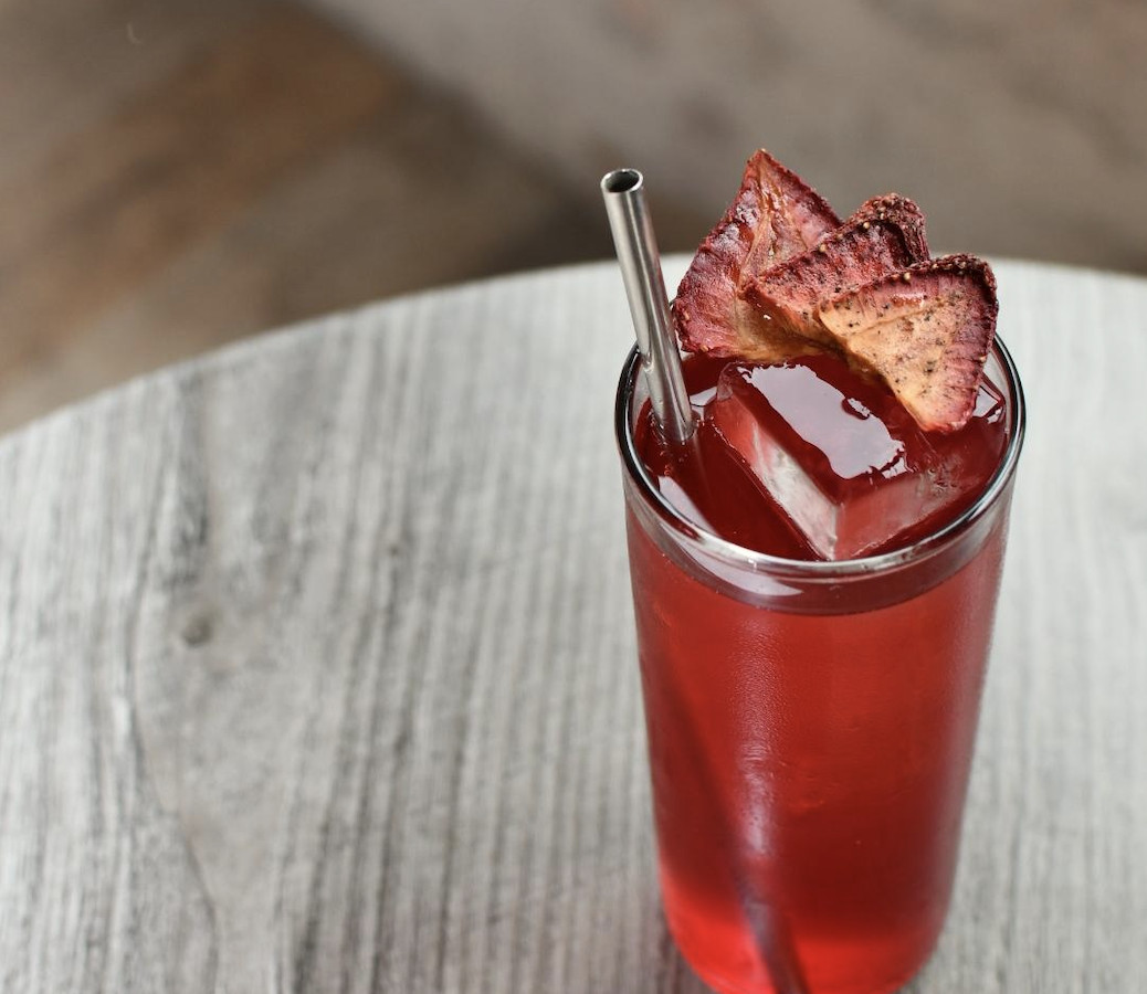 A bright red drink in a tall glass with a metal straw