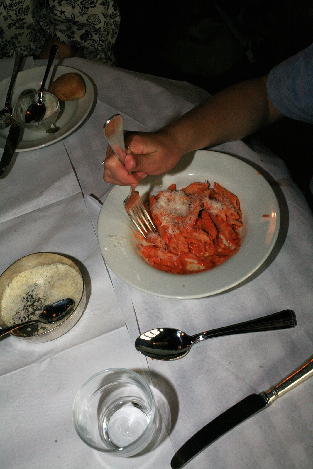 Penne alla vodka on a white plate on a table, with Parmesan scattered over the top. A diner sits in front of it, fork poised.