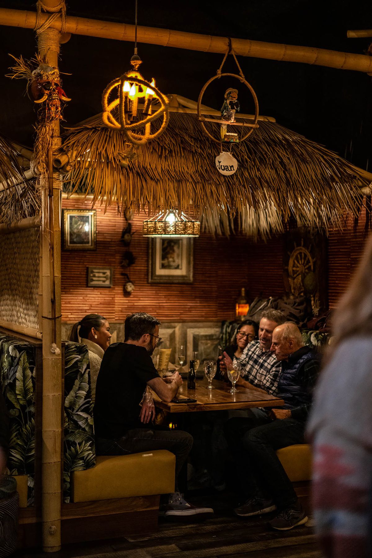 A thatched roof booth inside of a tiki restaurant.