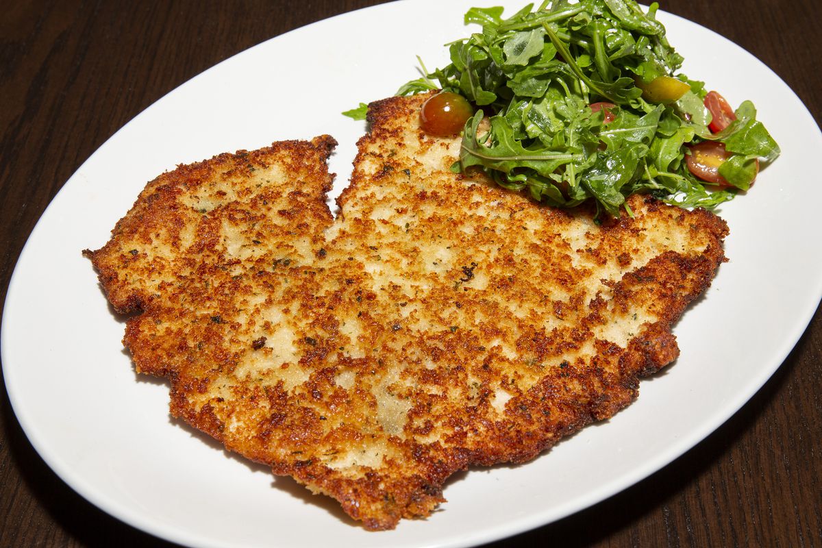 A plate of of thinly-pounded fried veal served with greens and cherry tomatoes.