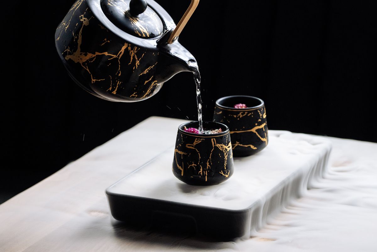 A tea pot pouring a cocktail into two small cups.