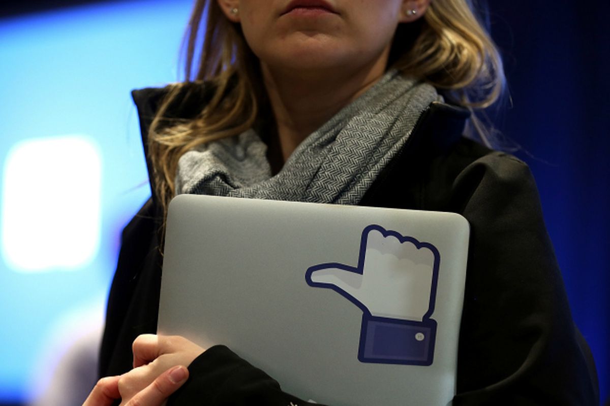 A woman holding a laptop with a picture of the Facebook thumbs up icon in it.
