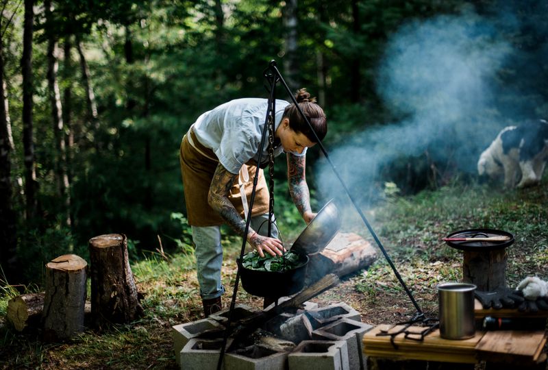 A chef cooks over a campfire in a clearing in the woods